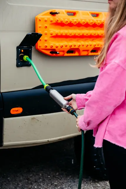 Eine Person füllt Frischwasser in einen Overlanding Campervan mit Wasserfilter und Bergebrett.