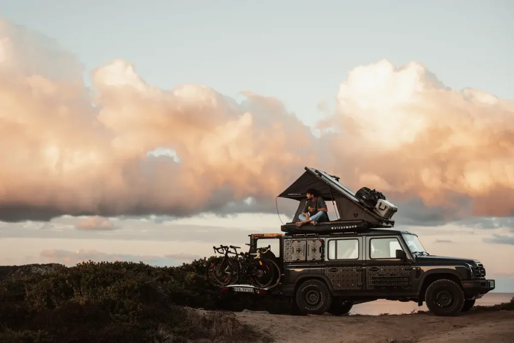 Ein 4x4-Geländewagen mit offenem Dachzelt und Fahrrädern beim Overlanding im Sonnenuntergang.