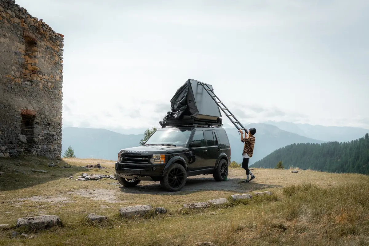 Ein schwarzer Land Rover Discovery 4x4 mit Dachzelt in den Bergen wird vorbereitet.