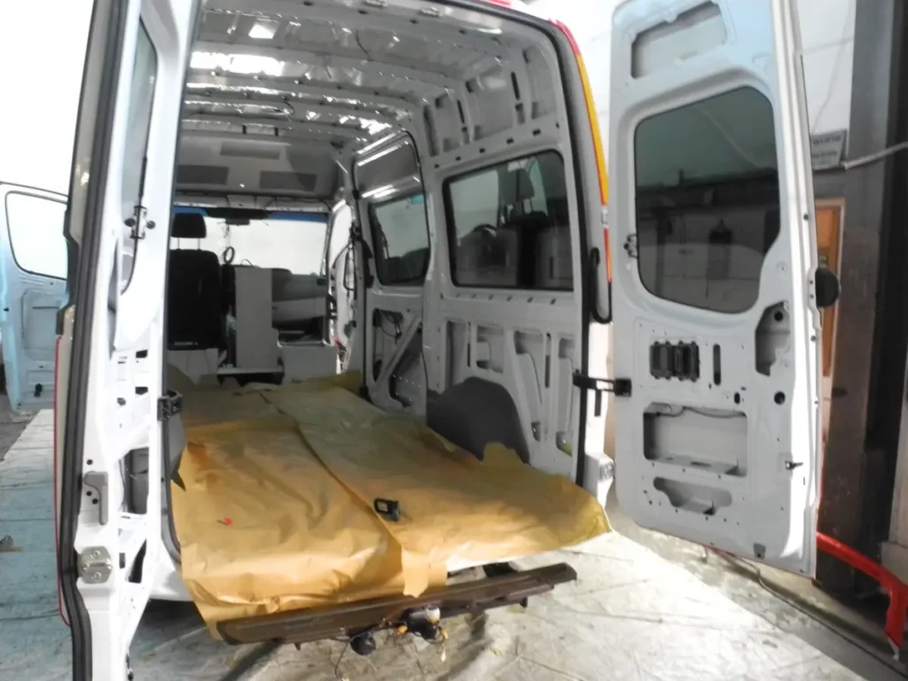 Innenansicht eines weißen Campervans während des Selbstausbaus mit geöffneten Hecktüren.