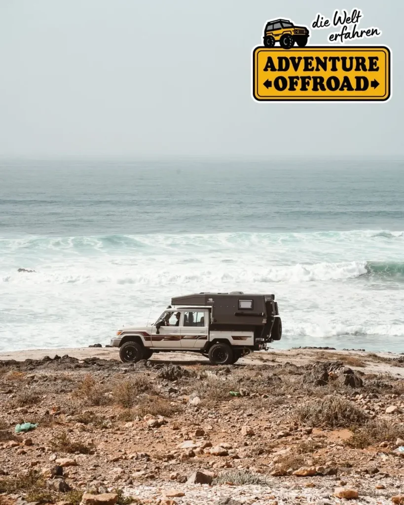 Weißes 4x4 Expeditionsmobil mit Wohnkabine parkt an felsiger Küste am Meer.