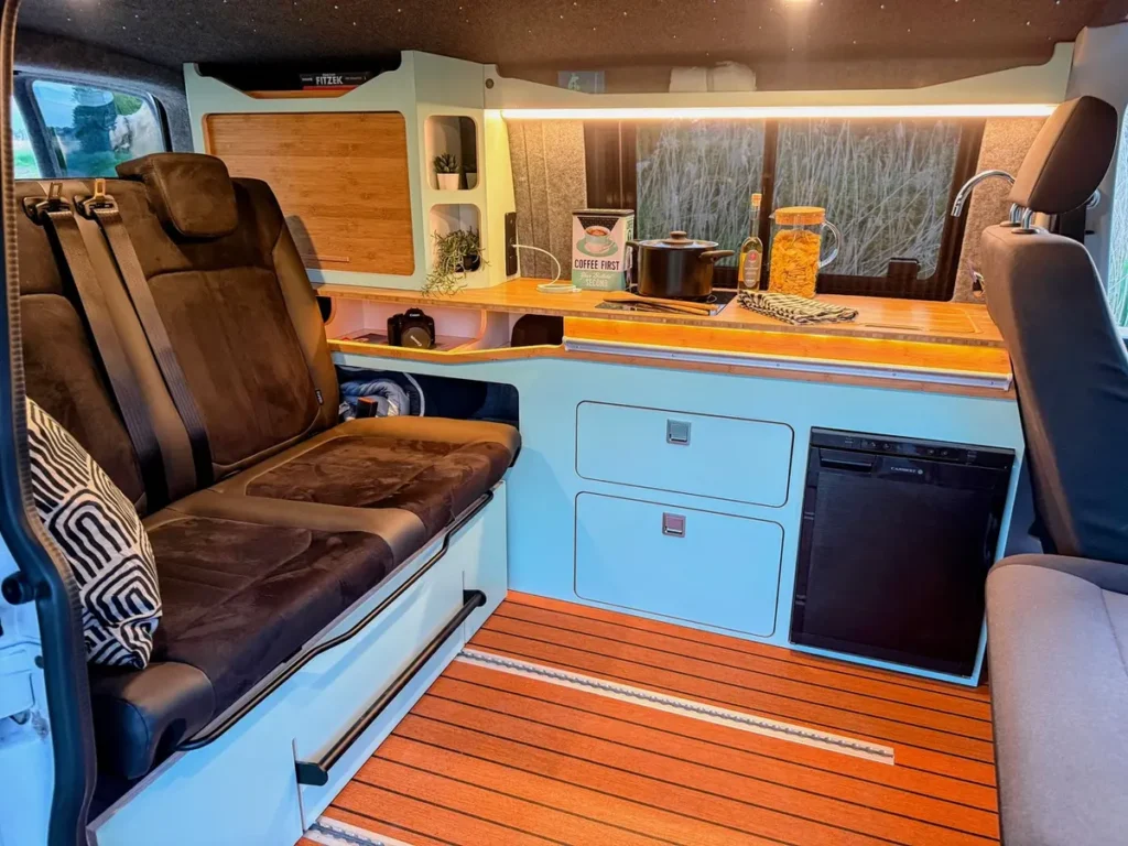 Moderner Campervan-Selbstausbau mit ausgestatteter Küche, Holzboden und bequemer Sitzbank.