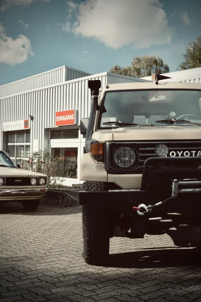Ein beiger Toyota Land Cruiser Expeditionsfahrzeug mit Snorkel und eine klassische Toyota Limousine.