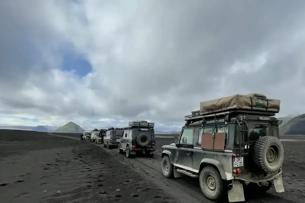 Mehrere 4x4-Expeditionsfahrzeuge mit Dachzelten fahren im Konvoi auf schwarzem Offroad-Boden.