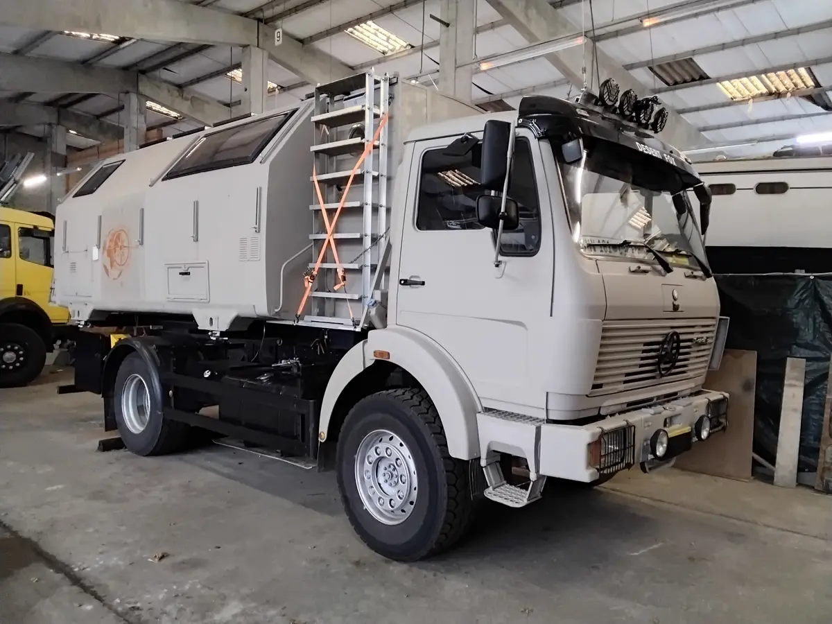 Graues Expeditionsmobil auf LKW-Basis mit Wohnkabine und Offroad-Bereifung in einer Halle.