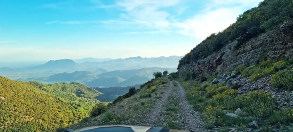 Eine Schotterpiste führt durch eine bergige Landschaft mit weitem Talblick.