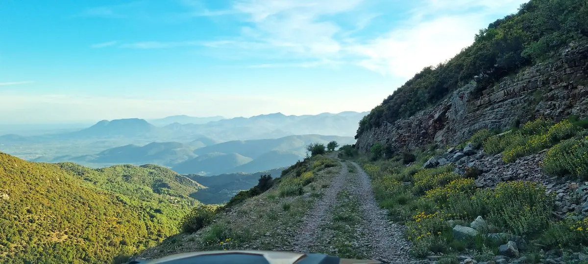 Eine Schotterpiste führt durch eine bergige Landschaft mit weitem Talblick.