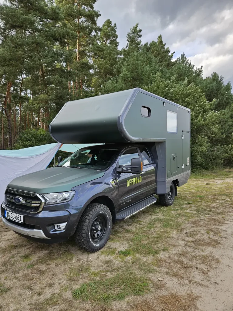 Offroad Ford Ranger mit dunkelgrüner Pick-up Wohnkabine am Waldrand.