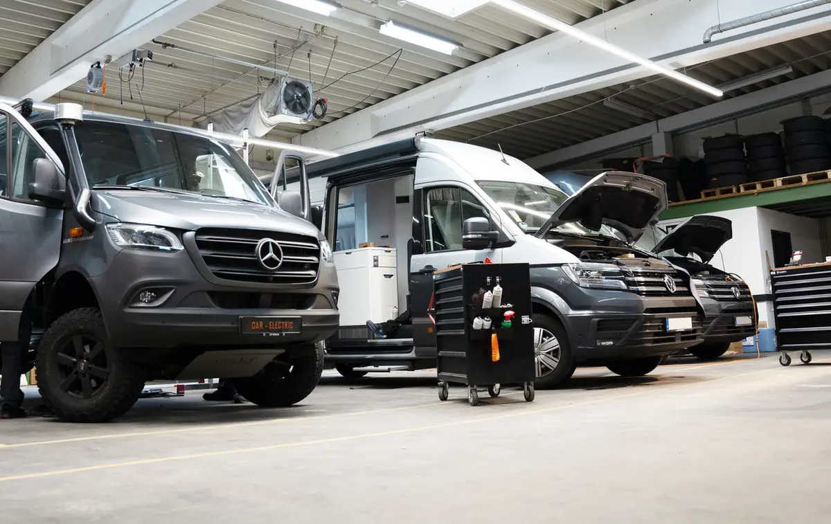 Werkstatt zeigt verschiedene Campervans und Offroad-Fahrzeuge, darunter einen 4x4 Sprinter, bei Umbau und Wartung.