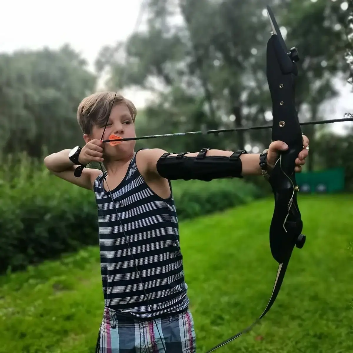 Ein junger Junge übt Bogenschießen im Freien mit einem schwarzen Bogen und Pfeil.