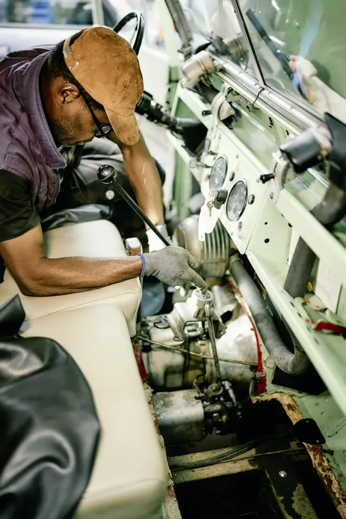 Ein Mechaniker mit Handschuhen prüft die Schaltung eines älteren Geländewagens von innen.