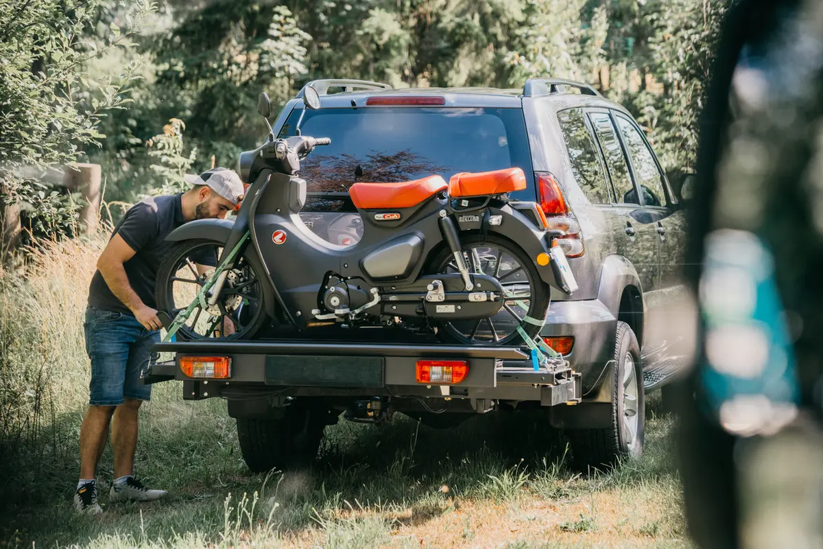 Ein Mann sichert ein kleines Motorrad auf einem Anhängerkupplungs-Träger an einem SUV.