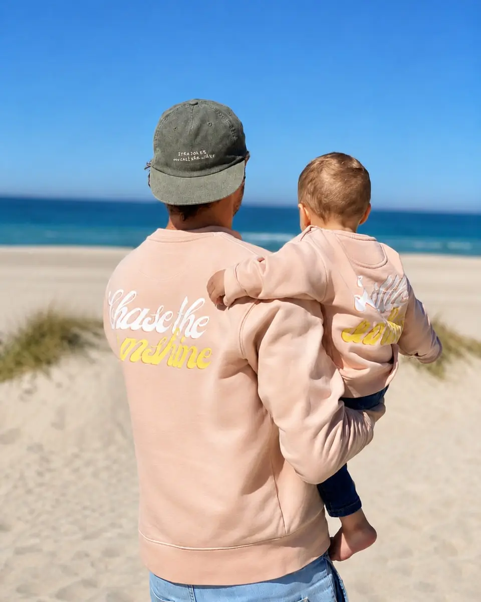 Vater hält Kind am sonnigen Strand mit Blick auf das blaue Meer.