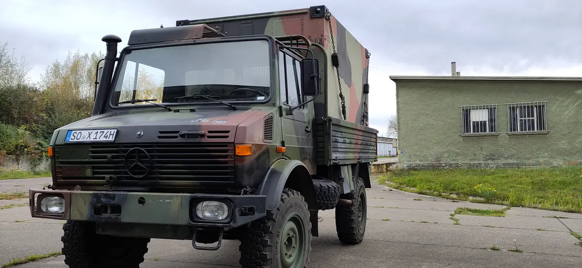 Ein getarnter Mercedes-Benz Unimog 4x4 Expeditions-LKW mit Kofferaufbau steht auf einem Gelände.