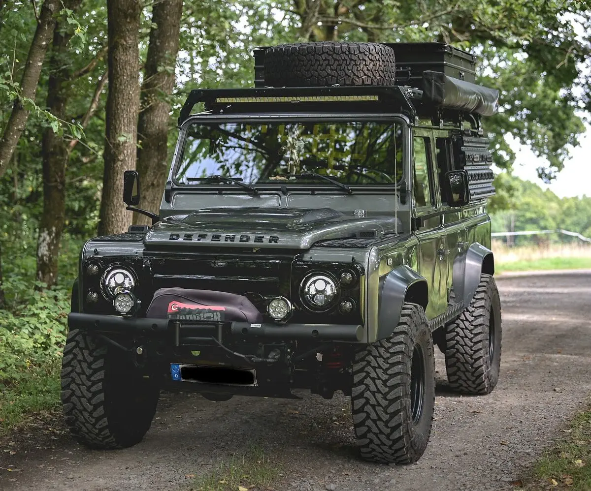 Ein dunkelgrüner Land Rover Defender als robustes 4x4 Expeditionsfahrzeug auf einem Waldweg.