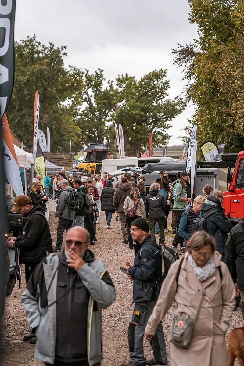 Besucher schlendern an verschiedenen Fahrzeugen mit Dachzelten und Expeditionsmobilen auf einem Outdoor-Treffen vorbei.
