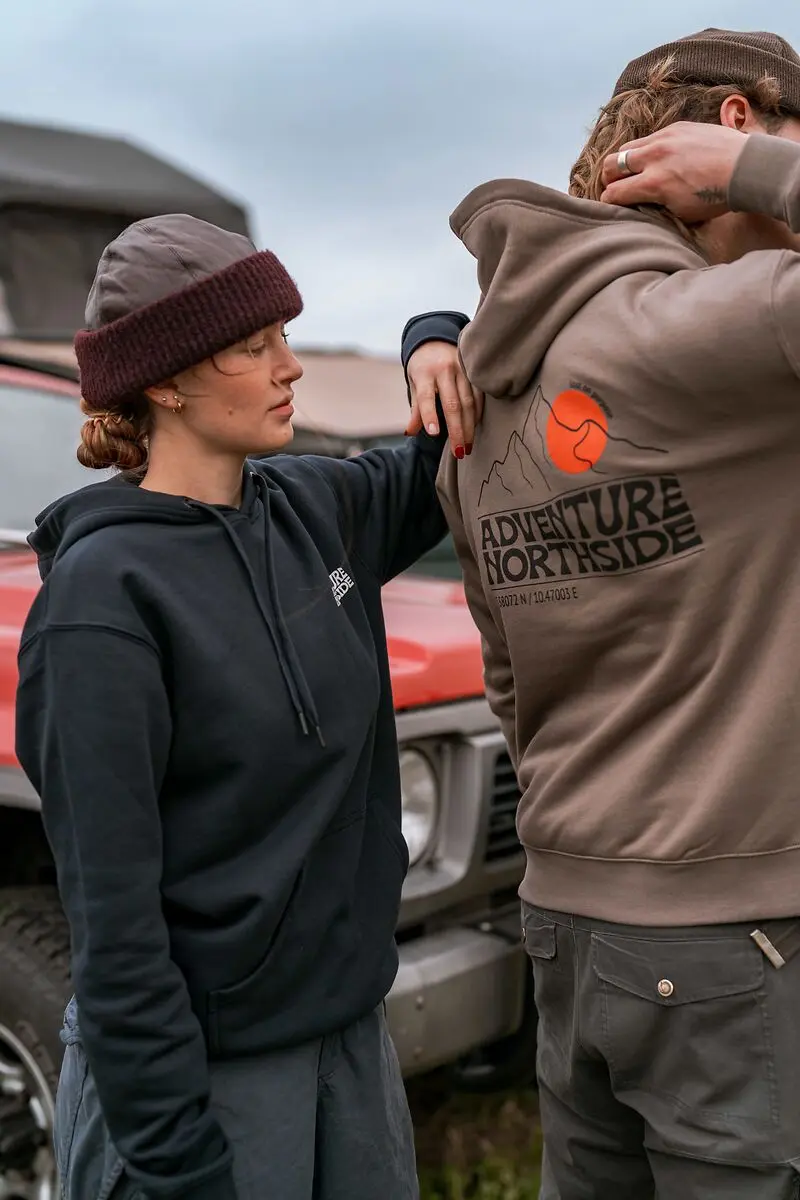 Zwei Personen in Outdoor-Kleidung stehen vor einem roten Expeditionsfahrzeug mit Dachzelt.