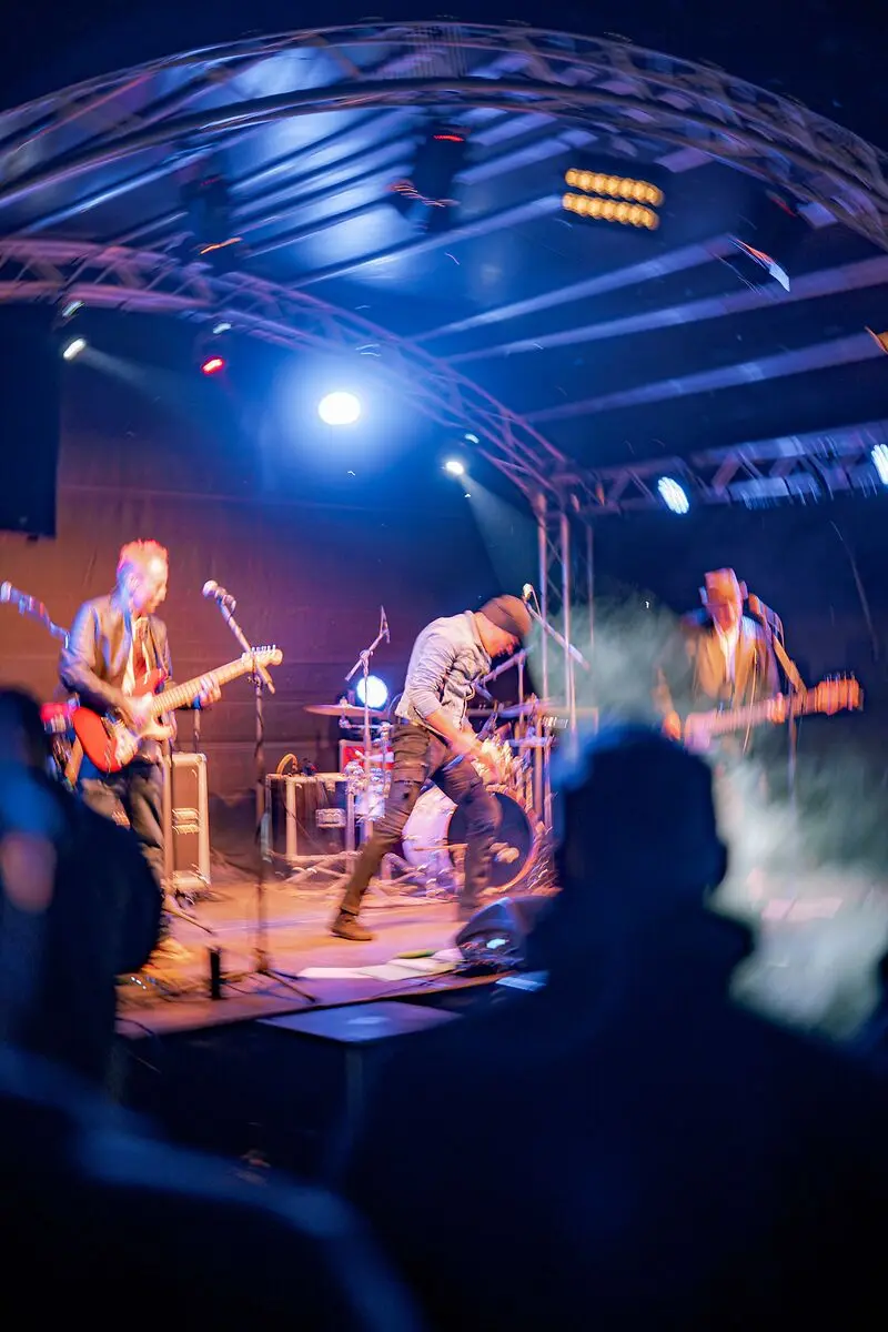 Eine Live-Band spielt auf einer Bühne, beleuchtet von blauen Scheinwerfern vor Publikum.