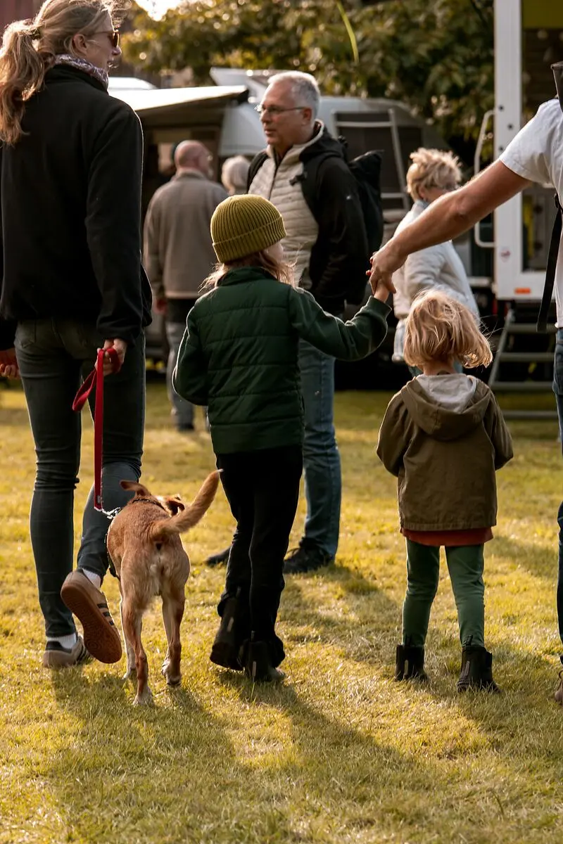 Familien mit Kindern und Hund auf einem Grasfeld vor Reisemobilen.