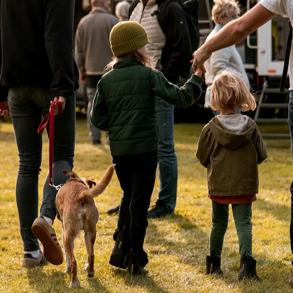 Zwei Kinder mit Hund und Erwachsenen auf einem grünen Outdoor-Gelände.