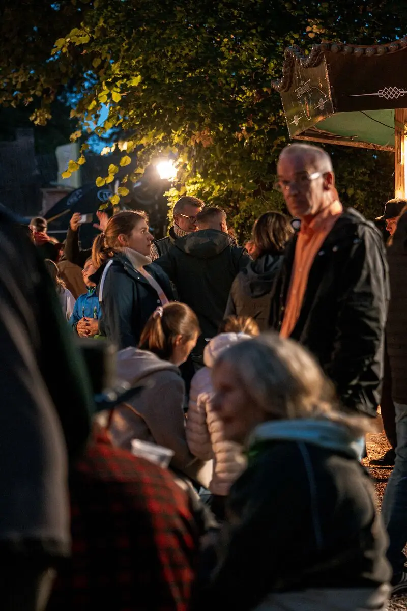 Abendliche Menschenmenge unter beleuchteten Bäumen, eine gemütliche Stimmung verbreitend.